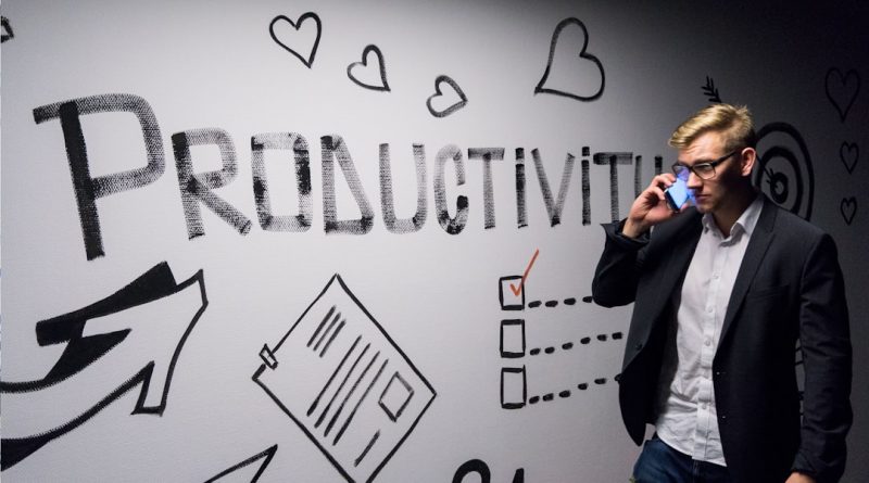 man holding smartphone looking at productivity wall decor - Photo by Andreas Klassen on Unsplash